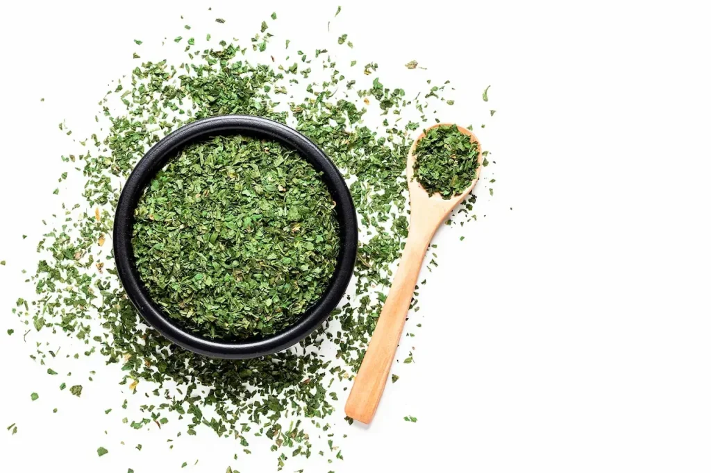 A Black Bowl and Wooden Spoon Filled with Dried Parsley